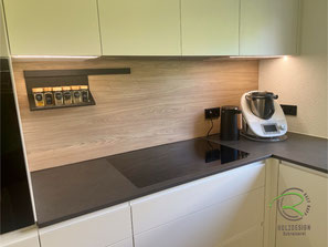 In anthraziter Keramik Arbeitsplatte flächenbündig eingebautes Induktionskochfeld, im Schrank versenkte Flachschirmhaube im Oberschrank, LED-Arbeitsplatzbeleuchtung, schwarzes Relingsystem mit heller Holzdekor Nischenplatte