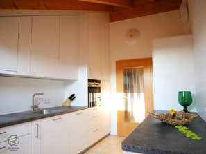 Küche mit Dachschräge und sichtbaren Holzbalken. Maßgefertigte weiße Schreinerküche mit raumhohen Hochschränken, Backofenhochschrank und optimal genutztem Stauraum unter der Dachschräge.