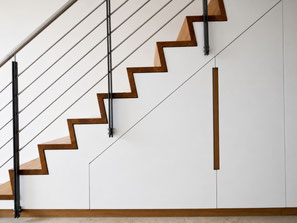 Garderobenschrank nach Maß unter einer Faltwerktreppe. Die innenliegende Garderobe nutzt den Raum unter der Treppe als Stauraum für Jacken, Taschen und Schuhe und greift die Eiche-Treppenstufen mit flächenbündigen Griffleisten auf.