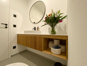 WC-Unterschrank nach Maß in Villingen-Schwenningen mit Eiche-Rillenoptik, offenem Ablagefach, Aufsatzwaschbecken und rundem Spiegel.
