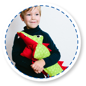 Kuscheltierkissen. Ein grünes Krokodilkissen beziehungsweise ein Drachenkissen im Arm eines 4-jährigen Jungen.