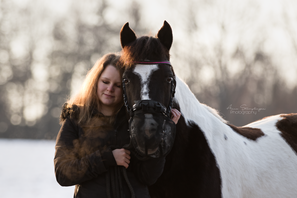 Pferd mit Besitzerin im Sonnenuntergang im Winter