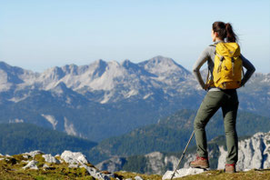 Wanderin in den Bergen als Symbol für körperliche Aktivität, Ausdauer und gesunde Muskulatur.