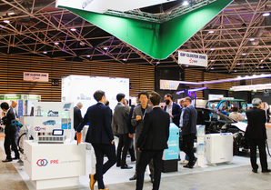 写真：展示会ブースで数名が立ち話や商談をしている様子。会場は来場者で賑わっている