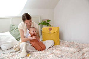 Mutter mit Baby im Schlafsack von LÄSSIG sitzend auf Elternbett (Deko Rolltop von LÄSSIG)
