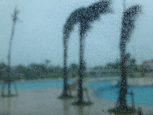 台風襲来中のプールサイドをガラス越しに屋内から撮影。ガラスに雨粒がびっしり.