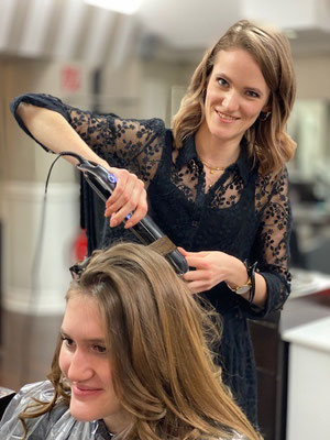 Eine freundlich lächelnde Friseurin wellt die Haare einer Kundin mit einem Glätteisen