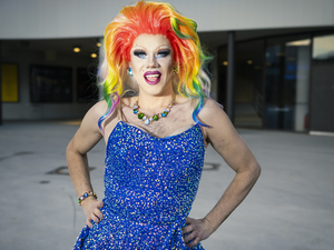 Eine Person mit buntem, rainbow-farbenem Haar und auffälligem Make-up trägt ein blaues, glitzerndes Kleid.