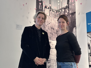 Zwei Frauen (Astrid Hirsch-von Borries und Saskia Holte) vor einer Ausstellung: eine im schwarzen Sakko, die andere im schwarzen Pullover und Jeans.