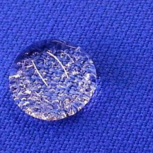 Von einem blauen und gewebten Textil abperlender dicker Wassertropfen.