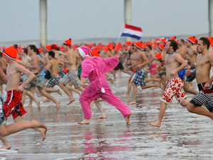 Menschen mit orangefarbenen Mützen rennen ins Meer bei Scheveningen, Den Haag