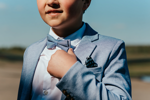 detail van jongen die speelt met het strikje van zijn kostuum in mooi zonlicht-communie-lentefeest-groeifeest-vormsel-kinderportret-by Fotografils-Ilse Wagemakers-fotograaf-Brasschaat