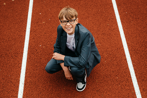 lachende jongen op een atletiekpiste in vogelperspectief-lentefeest-communie-vormsel-spontane kinderfotografie-Fotografils-by Ilse Wagemakers-fotograaf-Essen