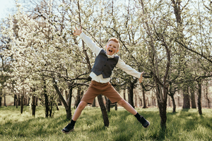 jongen die vrolijk springt met bomen in bloesem op de achtergrond-lentefeest-communie-groeifeest-spontane kinderfotografie-Fotografils-by Ilse Wagemakers-fotograaf-Essen