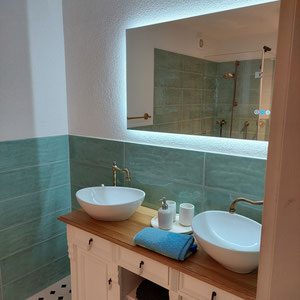Doppelwaschtisch mit Eichenplatte im Landhausstil in modernem Badezimmer mit türkisen Fliesen und großem beleuchtetem Spiegel
