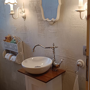 Romantische Gästebad mit nostalgischem Landhauswaschtisch "Loure" mit aufgesetztem Becken, darüber ein verzierter Spiegel mit bezaubernden Wandlampen
