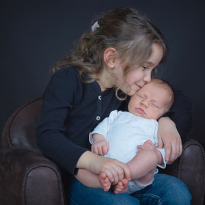 bébé dans les bras de sa grande soeur qui le couvre de bisous