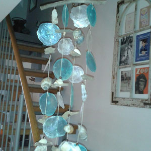 Maritimes Windspiel aus blauen und weißen Capizscheiben mit Schneckenhäusern am Treppenaufgang.