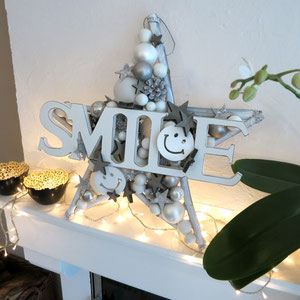 Weißer Stern mit SMILE Schriftzug mit Lichterkette auf dem Kaminsims arrangiert
