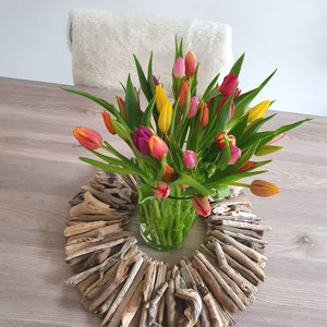 Brauner Treibholzkranz auf dem Tisch - in der Mitte steht eine Vase mit Tulpen.