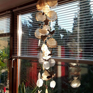 Gelb-Natur Capizwindspiel als Blickfang in einem großem Blumenfenster.