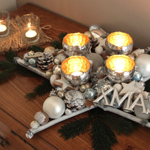 Tischdekoration im Stern Design - silberfarbiger Stern mit vier Windlichtern und XMAS - Schild auf Tannenzweige gelegt.