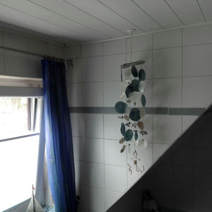 Blaues Windspiel im Badezimmer, farblich passend zu den blauen Vorhängen.