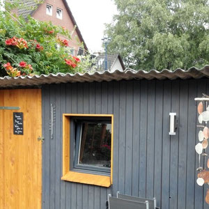 Windspiel aus treibholz und orange Capizscheiben vor dem Gartenhäuschen.