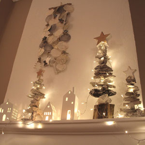Weiß-graues Capiz Windspiel mit weißen Treibholzbäumen, einer Lichterkette und Porzellanhäuschen dekoriert.