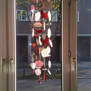 Windspiel in rot-natur im Wohnzimmerfenster, als Sichtschutz.