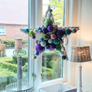 Fensterdekoration bestehend aus einer weißen Stehlampe, Kerzenleuchter und einem Glaskugel Stern in fröhlichen Farben.