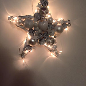 Weihnachtlicher Leuchtstern in weiß-silber an weißer Wand.