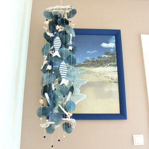 Windspiel mit blauen Capiz-Muscheln und Holzfischen vor maritimen Bild.