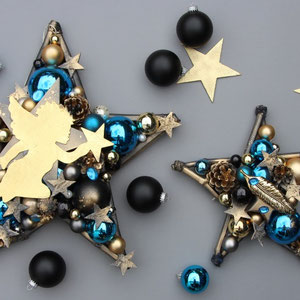 Deko-Sterne in gold - blau - schwarz mit Engel und Feder liegen auf einem grauen Untergrund.