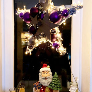 Violetter Stern mit eingearbeiteter Lichterkette im Fenster mit Weihnachtsmann dekoriert.