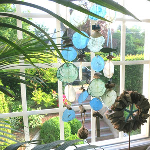 Windspiel mit Capicemuscheln und Treibholzkranz im Fenster dekoriert.