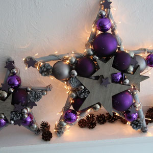 Ein kleiner 30 cm und ein großer Stern in 50 cm in violett - grau zusammen arrangiert. Beide Sterne sind mit grauen Holzsterne geschmückt.