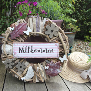 Treibholzkranz mit roten Holzblättern, grauen Blumen und rosa "Willkommen" Schild.