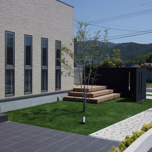 玄関前のタイル貼りスペースも庭の一部に取り込まれるデザインです。芝生は人工芝を採用しています。　岡山市北区Y様邸　フラワーチルドレン。