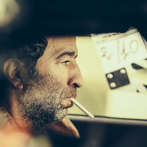 portrait de Slimane dazi dans une voiture en train de fumer une cigarette