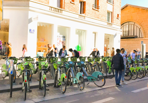 写真：パリの建物沿いに並ぶシェア自転車ステーション。利用者が自転車を選んでいる様子