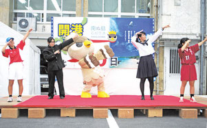 新空港開港の残歴板を前に「おかえり南ぬ島」に合わせて踊る「ぱいーぐる」や高校生たち=27日夕、市役所第2駐車場