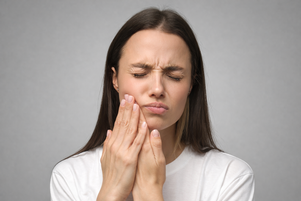 Mujer con dolor dental agudo tocando la mejilla al despertar, síntoma de apretamiento nocturno