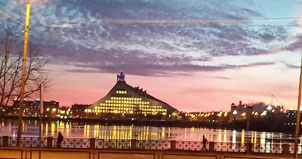 National Library of Latvia seen from across the Daugava River at sunset with a pink sky and yellow lights inside the building