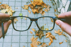 A pair of glasses held out in front of a person's eyes. The ground is covered in bricks with leaves on top. Taken together with the text, the image suggests that mindfulness helps people gain fresh perspective on everyday life.