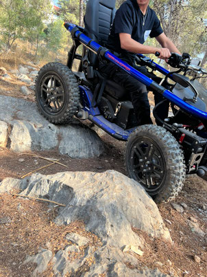 A metallic blue TerrainHopper, driven by a young man in a dark blue t-shirt, navigating a rocky trail. over large boulders in a trail.