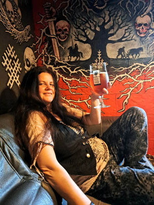 Girl with long dark hair holding a glass of beer against background of pagan symbols in Riga