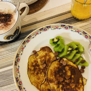 table de petit-déjeuner avec un café, un jus de fruits et une assiette de pancakes et kiwis