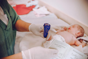 Baby nach der Geburt mit blauem Fuß für den Fußabdruck.