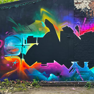 Bunte Farben strahlen auf einer mit Graffiti bemalten Wand. Leuchtende Farbverläufe umranden einen schwarzen Ohm Schriftzug.    